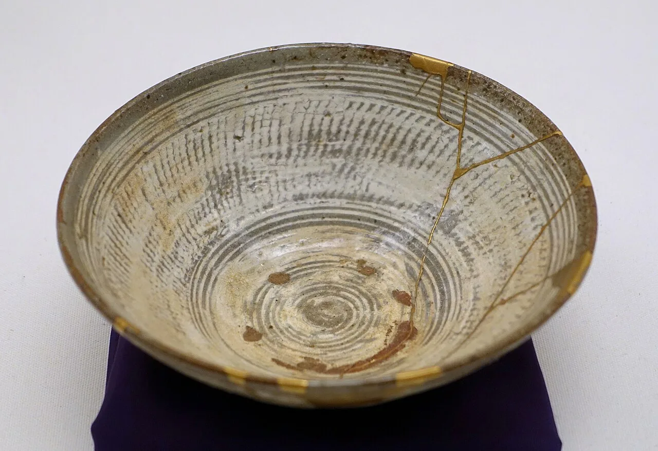 A Korean ceramic bowl whose cracks have been mended with gold lacquer, resting on a purple cloth